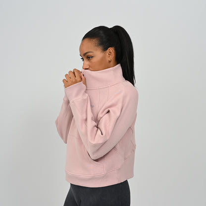 Close-up shot of model adjusting the zipped high collar on the dusty pink Hybryd Monterey half zip sweatshirt