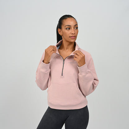 Front pose of model in the dusty pink Hybryd Monterey half zip sweatshirt with hands in kangaroo pocket