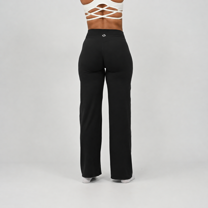 A pilates model wearing black wide-leg pants and white socks, shown from the waist down from the rear against a light gray studio background. From activewear brand Hybryd