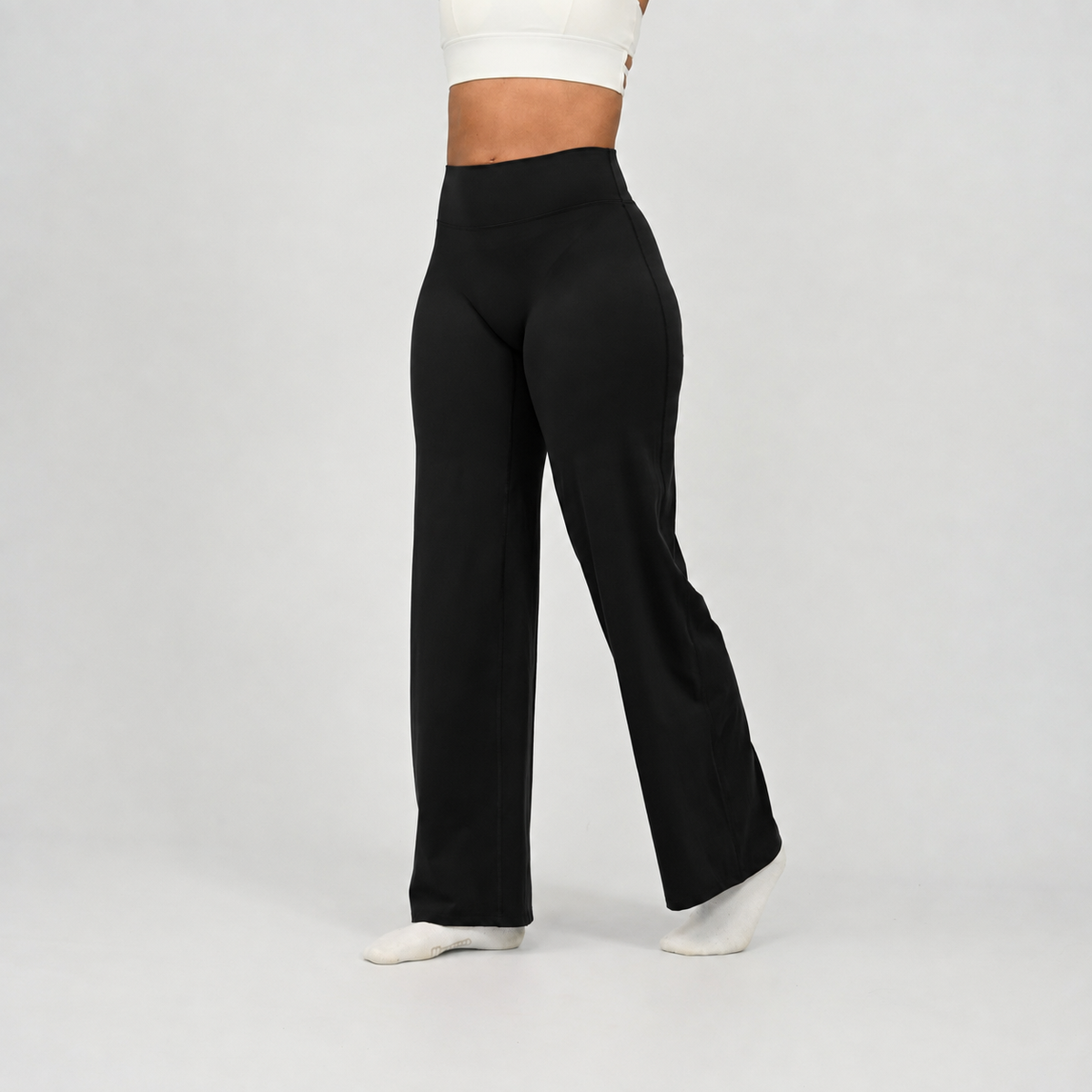 A pilates model wearing black wide-leg pants and white socks, shown from the waist down in a side profile against a light gray studio background. From activewear rand Hybryd