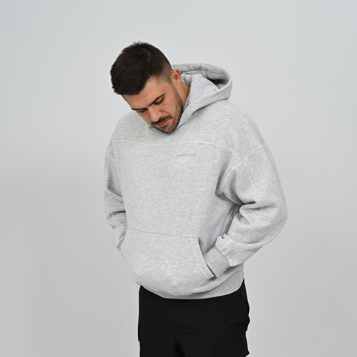 Three-quarter angle of male model wearing the grey Hybryd Palmer drop shoulder hoodie looking down